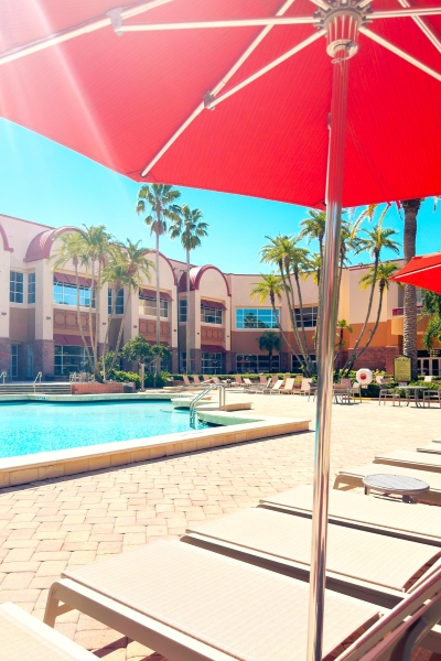 An open red umbrella shades lounge chairs by a pool at Rosen Centre in Orlando. 