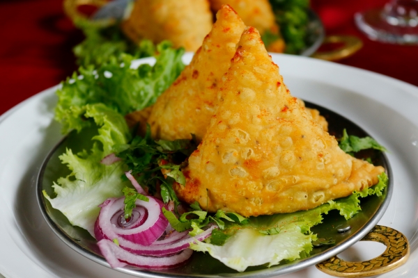 Two triangular fried samosas, a staple at Indian restaurants, on a bed of lettuce and red onion.