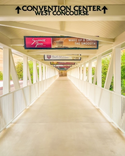 A clear, clean walkway with white railings and hanging advertisements overhead with a sign and arrows leading to the OCCC.