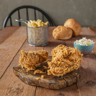A wooden table set with fried chicken, French fries, rolls, and a bowl of cole slaw.