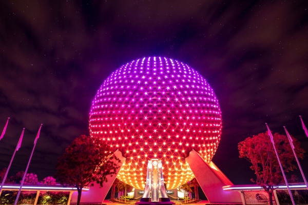 The glowing Spaceship Earth ball at EPCOT glowing pink and orange at night.