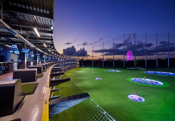 A large covered golf bay overlooking a target course at twilight.