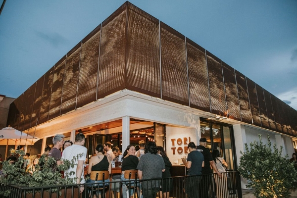The corner of a building with guests sitting at an outdoor patio in front of a sign that reads Tori Tori.