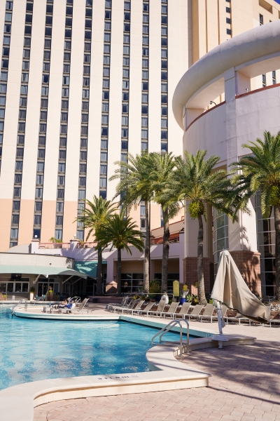 The corner of a swimming pool surrounded by tall buildings and palm trees.