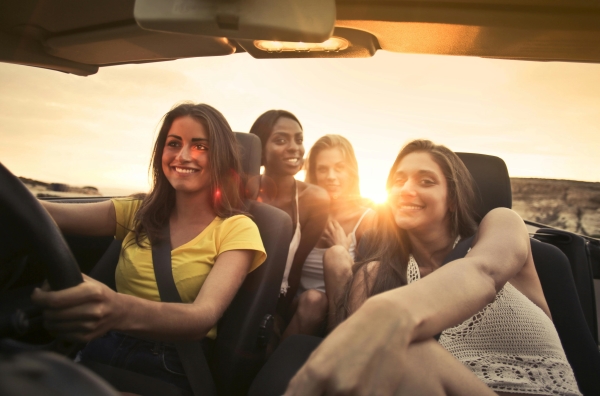 Four young women driving in a convertible with the sun setting behind them. 