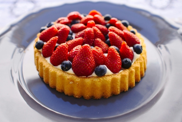 A beautiful fruit tart topped with strawberries and blueberries on a blue plate.