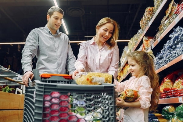 A man, woman, and girl put items into a grocery cart in a grocery store.