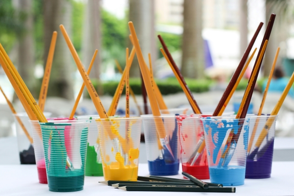 Plastic cups full of colorful paint with paintbrushes protruding from each one.