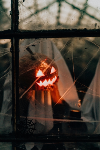 A sinister jack-o-lantern glowing surrounded by cobwebs and tattered fabric through a dusty window pane.