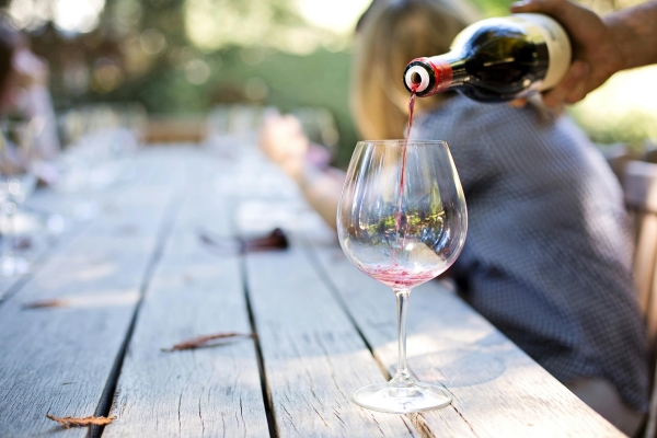 At an outdoor table, a hand pours red wine into an empty wine glass. 