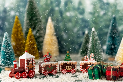 A close-up of a toy gingerbread train in a snowy forest of bottle brush trees. 