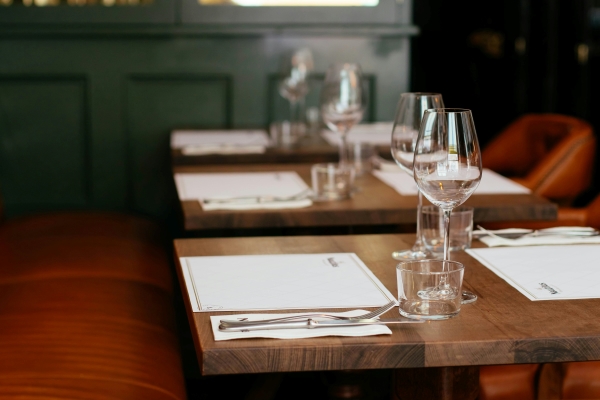 Three wooden tables with a red booth seat set with menus, silverware, and wine glasses.