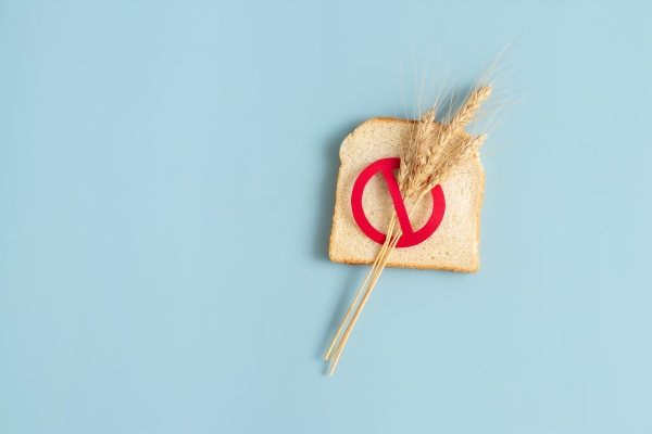  A slice of bread with a sprig of wheat and a red circle with a line through it resting on a light blue background.