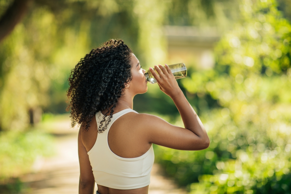 A woman in a sports bra outdoors drinks a bottle of water. 