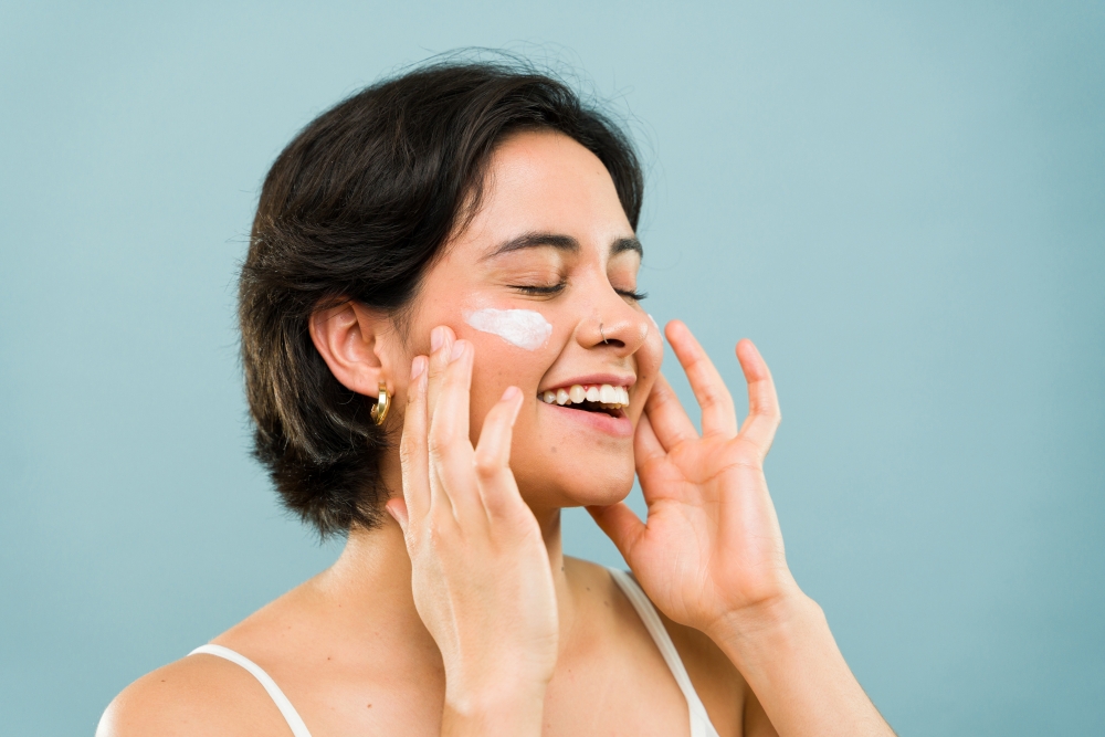 A smiling woman put moisturizer on her cheeks, an essential part of skincare. 