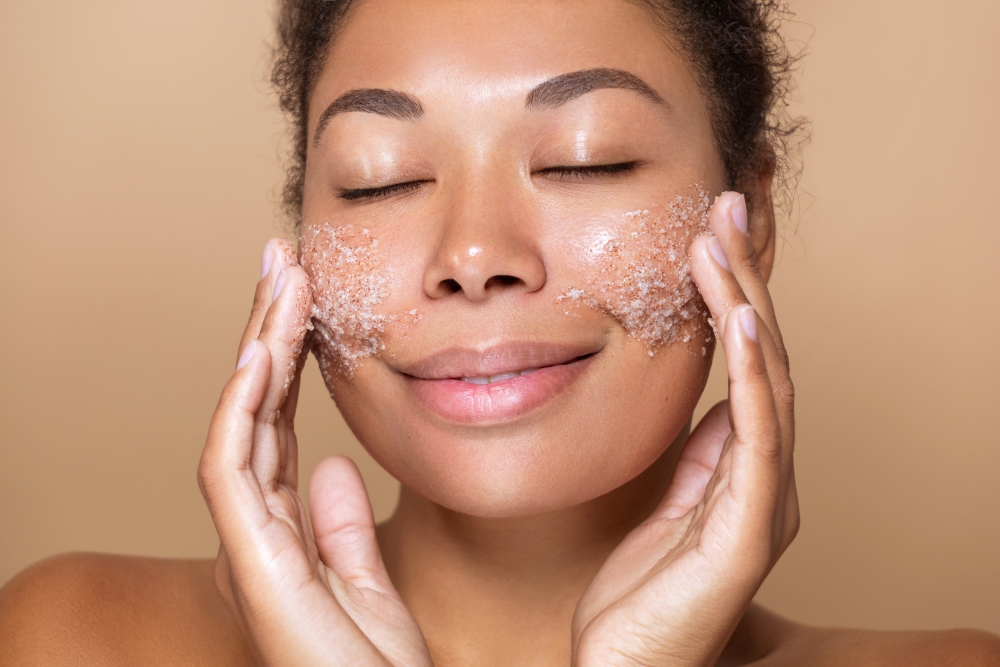 A close-up of a woman's face, which is is exfoliating while smiling. 