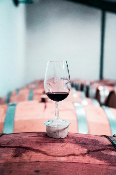 A glass of red wine balances on the cork of a wine barrel. 